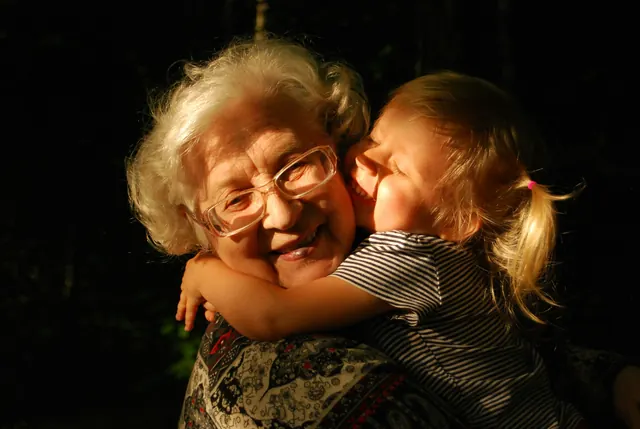 An elderly woman with white hair and glasses hugging a young child